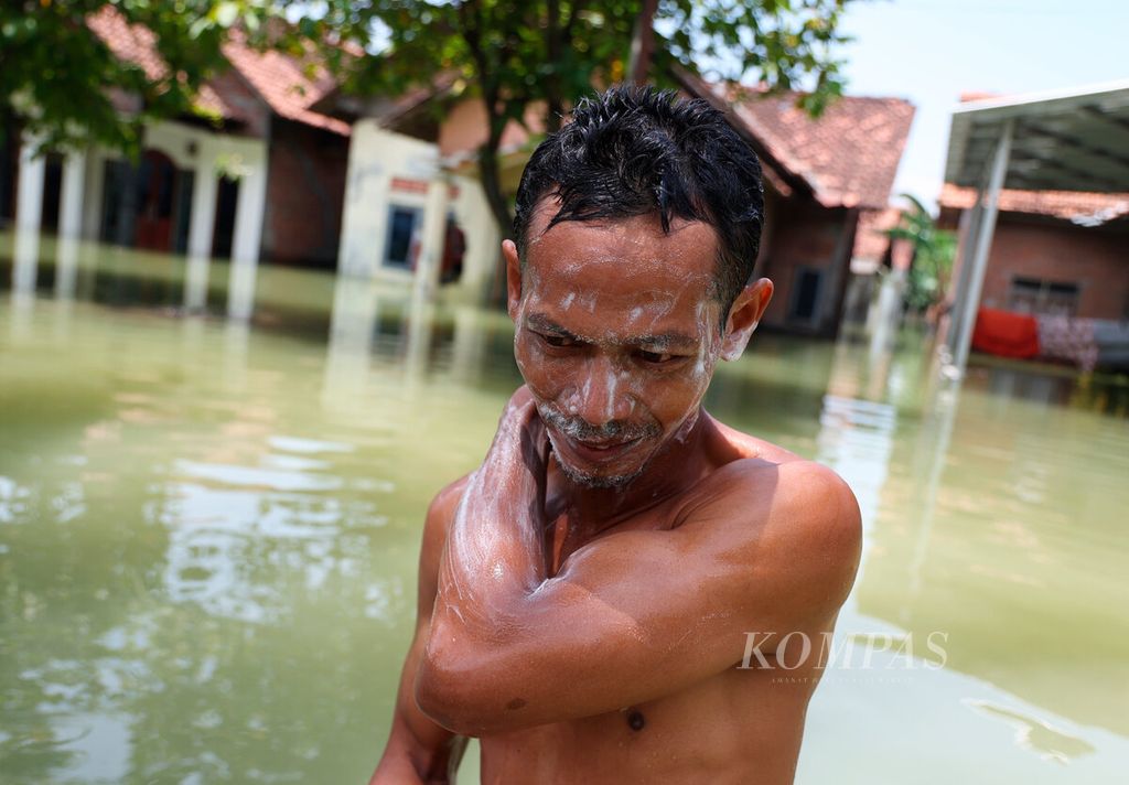 Warga mandi dengan air banjir yang menggenangi permukiman di Desa Cangkring Rembang, Kecamatan Karanganyar, Kabupaten Demak, Jawa Tengah, Selasa (19/3/2024). 