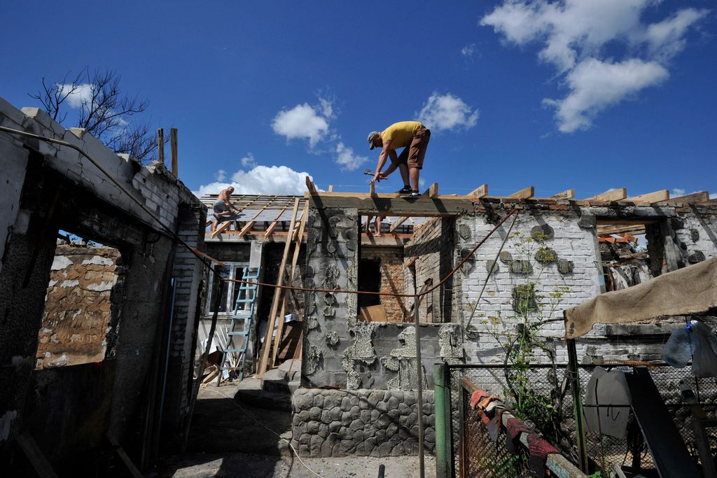Seorang sukarelawan membetulkan atap rumah yang didiami seorang perempuan lanjut usia di Desa Zalissya, Kyiv, Jumat (22/7/2022). Rumah ini rusak akibat serangan artileri pasukan Rusia. 