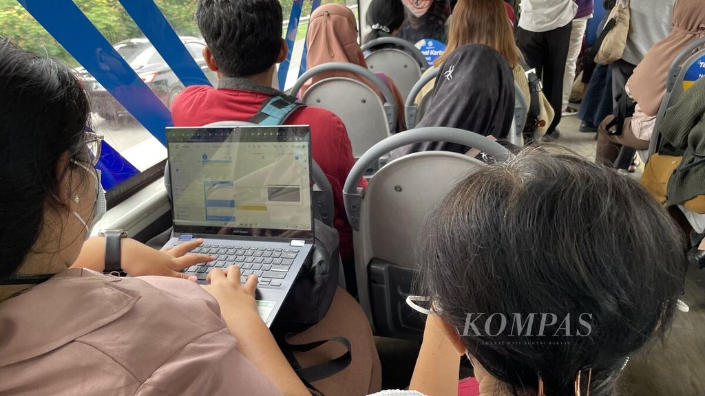 Seorang pekerja muda terpantau membuka laptop di dalam bus Transjakarta sekitar pukul 12.00, Senin (8/1/2024), untuk mengurus pekerjaannya. 