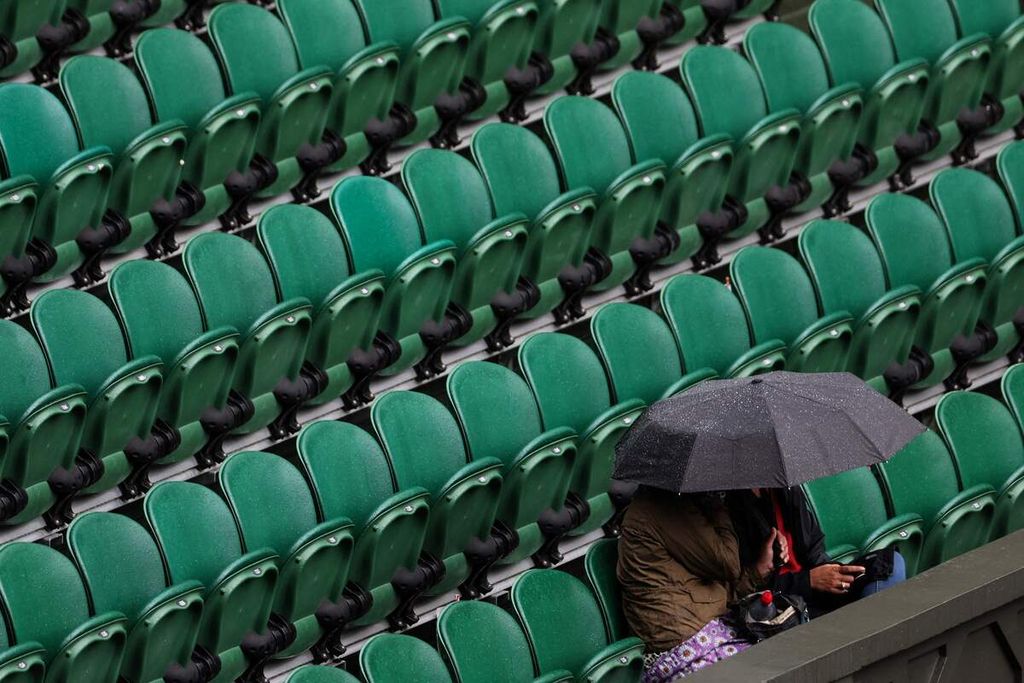 Penonton menggunakan payung saat turun hujan pada pertandingan antara Rafael Nadal dan Ricardas Berankis di All England Tennis Club, Wimbledon, Kamis (30/6/2022). Para petenis peserta turnamen Grand Slam Wimbledon menjadi waspada setelah tiga petenis unggulan tunggal putra positif Covid-19 dan mengundurkan diri dari turnamen. 