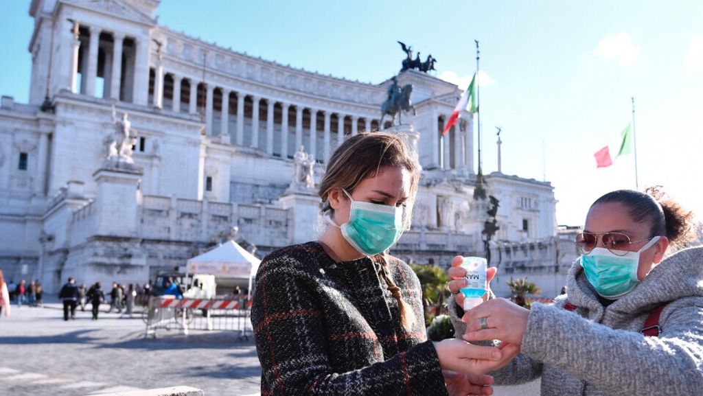 Wanita yang memakai masker mendisinfeksi tangan mereka di pusat Piazza Venezia, Roma, Italia, Minggu, 8 Maret 2020.  