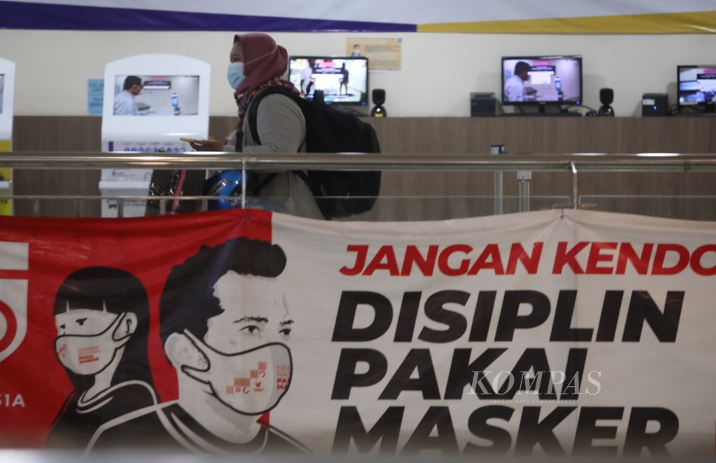 Calon penumpang melintas di depan spanduk imbauan protokol kesehatan yang terpasang di kawasan Terminal Terpadu Pulo Gebang, Jakarta, 26 Desember 2021. 