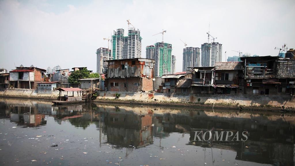 Permukiman kumuh di bantaran saluran Sunter dengan latar belakang pembangunan hunian vertikal, Jakarta Utara, beberapa waktu lalu. Pertumbuhan hunian mewah dan apartemen yang berimpitan dengan permukiman padat dapat memicu kesenjangan sosial.