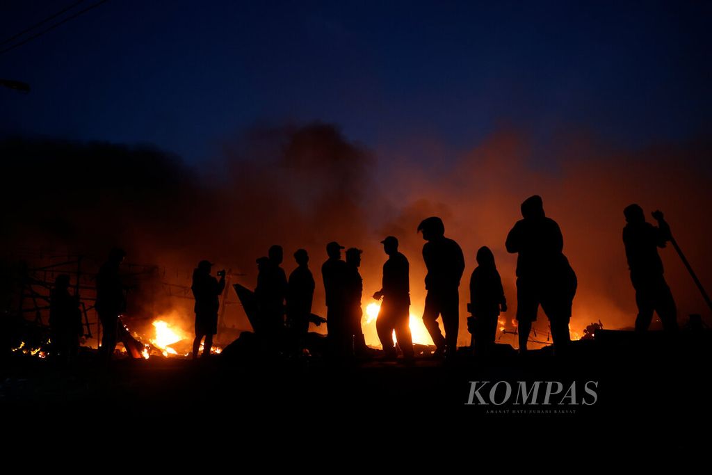 Warga dengan latar belakang kobaran api yang membakar puluhan kapal nelayan di Pelabuhan Perikanan Pantai Tegalsari, Kota Tegal, Jawa Tengah, Selasa (15/8/2023). Kebakaran yang terjadi sejak Senin malam tersebut meluluhlantakkan 52 kapal nelayan. 