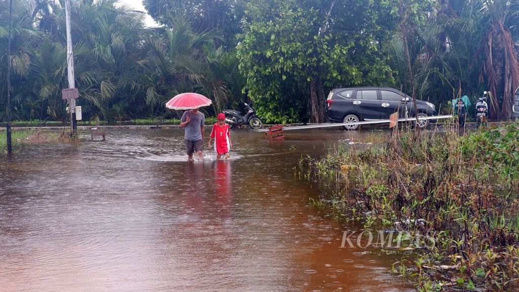 Warga melintasi genangan air di salah satu kompleks perumahan warga di Kelurahan Sungai Lulut, Kecamatan Banjarmasin Timur, Kota Banjarmasin, Kalimantan Selatan, Jumat (15/1/2021). 