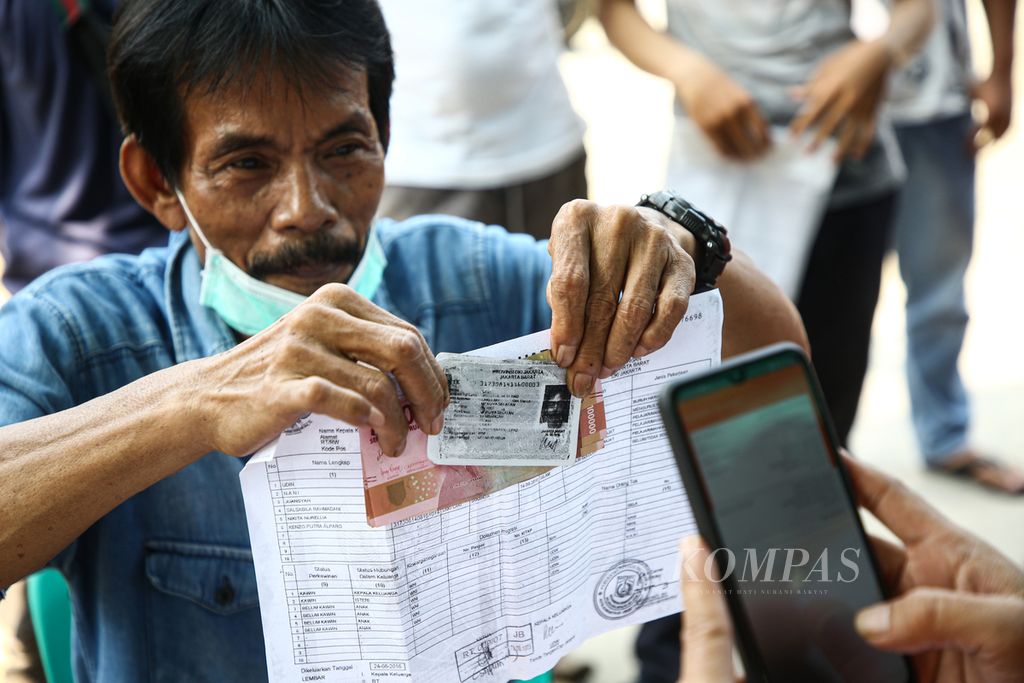 Warga memperlihatkan uang yang diterimanya untuk difoto petugas saat pembagian bantuan sosial tunai (BST) di kawasan Meruya Selatan, Kembangan, Jakarta Barat, Minggu (25/7/2021). 