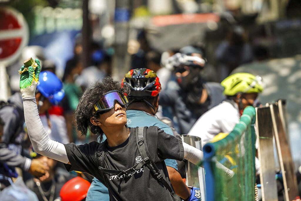 Pengunjuk rasa berancang-ancang untuk melempar ke arah polisi yang menjaga unjuk rasa di Yangon, Myanmar, Selasa (2/3/2021). Demonstrasi menentang kudeta militer di beberapa kota di Myanmar kembali dilanjutkan pada Selasa.