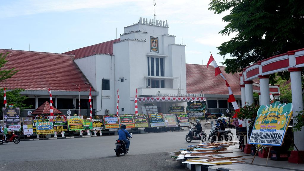 Warga melintas di depan Balai Kota Banjarbaru, Kalimantan Selatan, yang penuh dengan karangan bunga, Selasa (11/8/2020). Sehari sebelumnya, Wali Kota Banjarbaru Nadjmi Adhani meninggal dunia di Banjarmasin akibat menderita Covid-19.