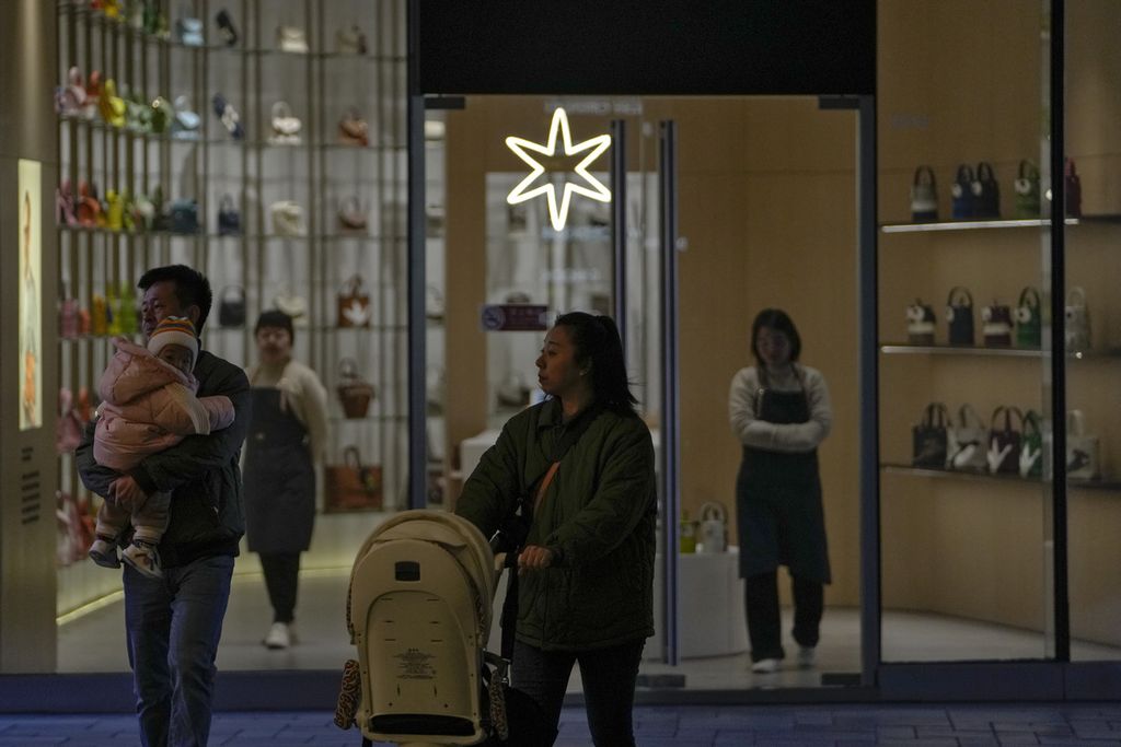 Sepasang suami istri dengan anaknya melewati pegawai toko yang sedang menunggu pelanggan di butik tas di pusat perbelanjaan luar ruangan di Beijing, China, pada 12 November 2023. 