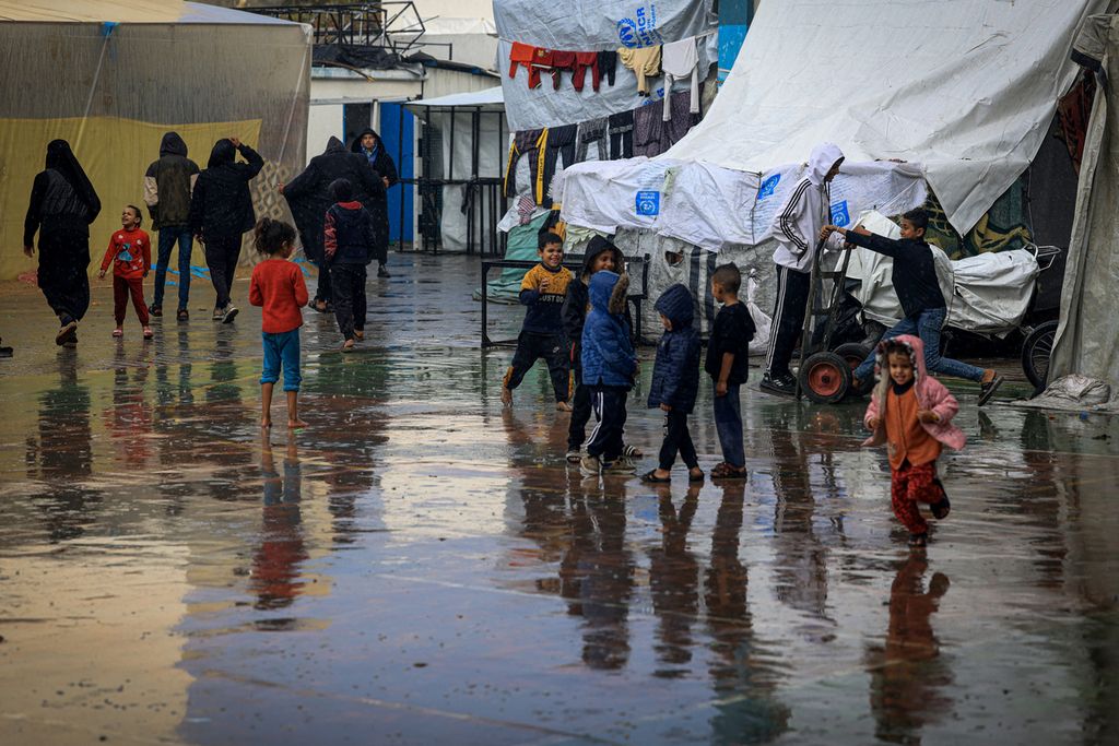 Anak-anak Palestina bermain di tengah hujan di kamp pengungsi di Rafah, Jalur Gaza, tempat sebagian besar warga sipil mengungsi saat pertempuran berlanjut antara Israel dan Hamas, Selasa (12/12/2023). 
