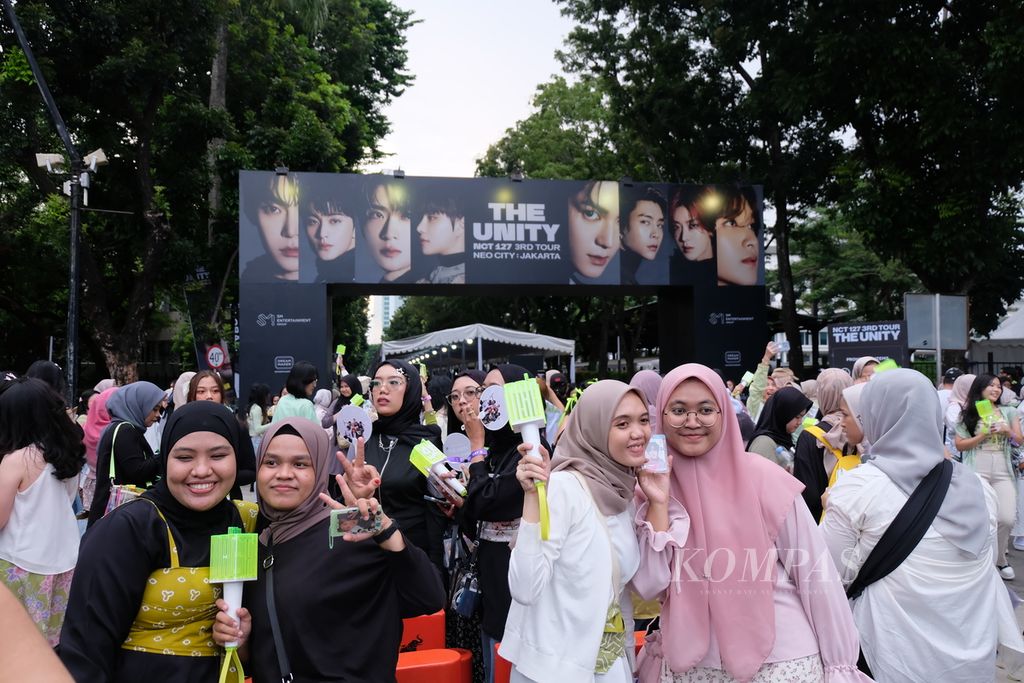 Sejumlah penonton berpose di gerbang lokasi konser grup musik Korea Selatan, NCT 127, di Stadion Indonesia Arena di kompleks Gelora Bung Karno, Jakarta, Sabtu (13/1/2024).  
