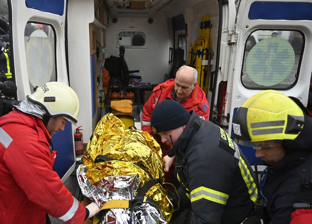 Tim penyelamat membawa seorang perempuan dengan ambulans setelah mengevakuasinya dari puing-puing bangunan tempat tinggal yang hancur pasca-serangan rudal di Dnipro, Ukraina, Minggu (15/1/2023).