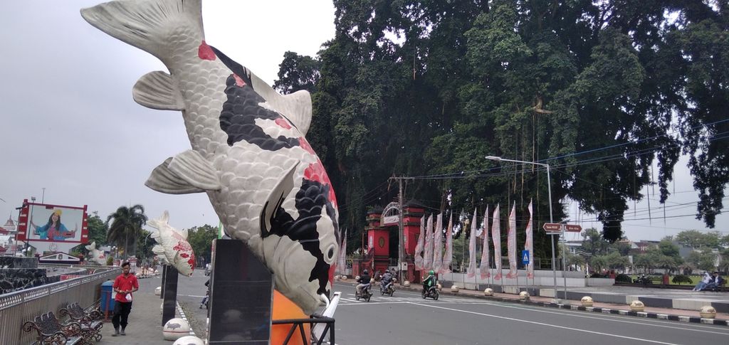 Seorang warga berjalan di trotoar yang ada di belakang patung ikan koi yang menjadi maskot Blitar, di jalan protokol Kota Blitar, Jawa Timur, 21 Desember 2021.