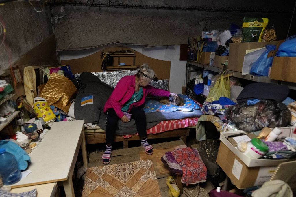 Seorang perempuan memelihara seekor anjing di ruang bawah tanah bangunan tempat tinggal yang rusak tempatnya tinggal di Avdiivka, Donetsk, pada 28 Juni 2023.