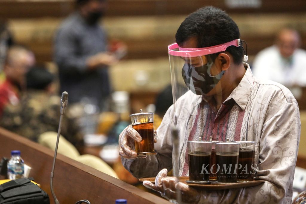 Petugas mengenakan masker dan pelindung wajah saat menyiapkan minuman untuk peserta rapat dengar pendapat antara anggota Komisi II DPR dan Komisi Pemilihan Umum, Badan Pengawasan Pemilu, dan Kementerian Dalam Negeri di Kompleks Gedung Parlemen, Senayan, Jakarta, Senin (22/6/2020). 