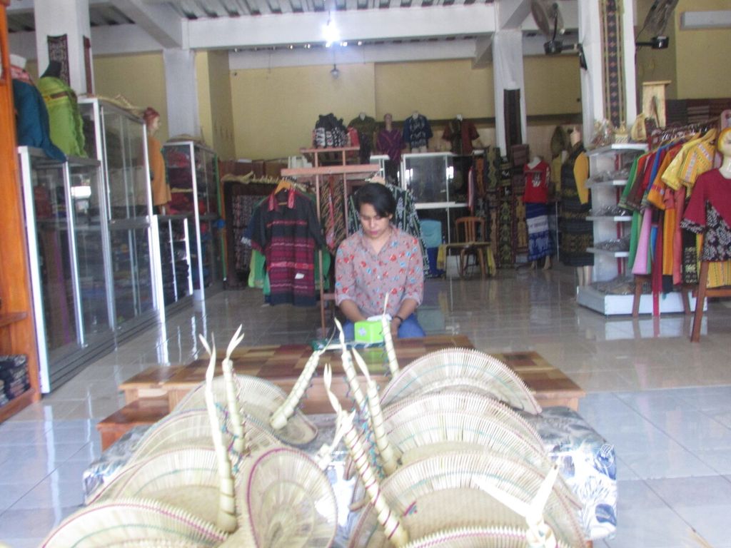 Asti (23), seorang karyawan di usaha mikro, kecil, dan menengah (UMKM) kerajinan tenun ikat Ina Ndao di Kupang, Nusa Tenggara Timur, Senin (10/5/2021), bekerja menggunting kertas untuk label setiap produk topi Tii Langga di depannya. Karena pandemi Covid-19, upah karyawan di tempat ini disesuaikan dengan pemasukan.