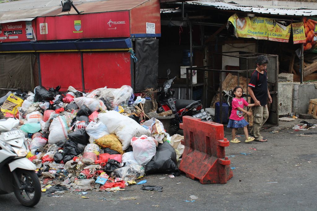 Seorang warga bersama anak kecil melewati tumpukan sampah di salah satu sudut Pasar Cicadas, Kota Bandung, Jawa Barat, Minggu (5/11/2023). 