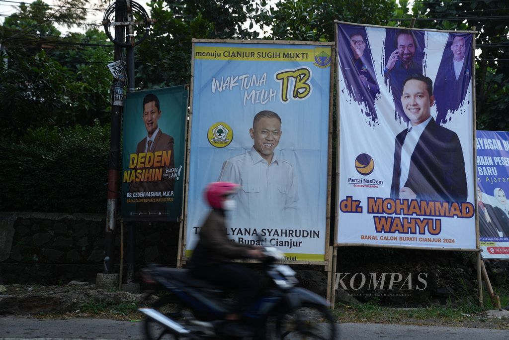 Warga melintasi baliho bergambar bakal calon bupati Cianjur di Kecamatan Sukaluyu, Cianjur, Jawa Barat, Kamis (18/7/2024). Pemilihan umum Bupati Cianjur 2024 dilaksanakan pada 27 November 2024 untuk memilih Bupati Cianjur periode 2024&ETH;2029. KOMPAS/AGUS SUSANTO (AGS) 19-7-2024