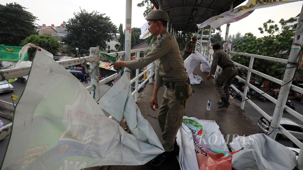 Sejumlah petugas Satpol PP menertibkan spanduk alat peraga kampanye (APK) yang melanggar aturan di jembatan penyeberangan orang (JPO) di kawasan Prumpung, Cipinang Besar, Jakarta Timur, 15 Maret 2019.