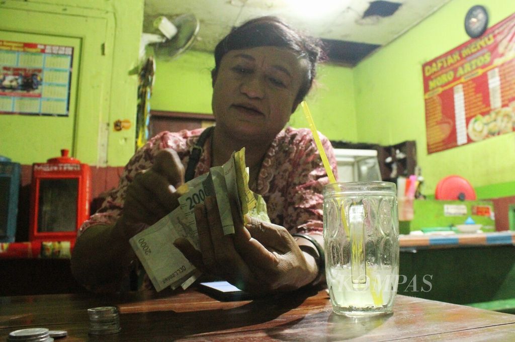 Transpuan pengamen, Rully Mallay (62), menghitung uang hasil mengamen di warung-warung lesehan di bawah Jembatan Layang Janti, DI Yogyakarta, Rabu (20/7/2022) malam. 