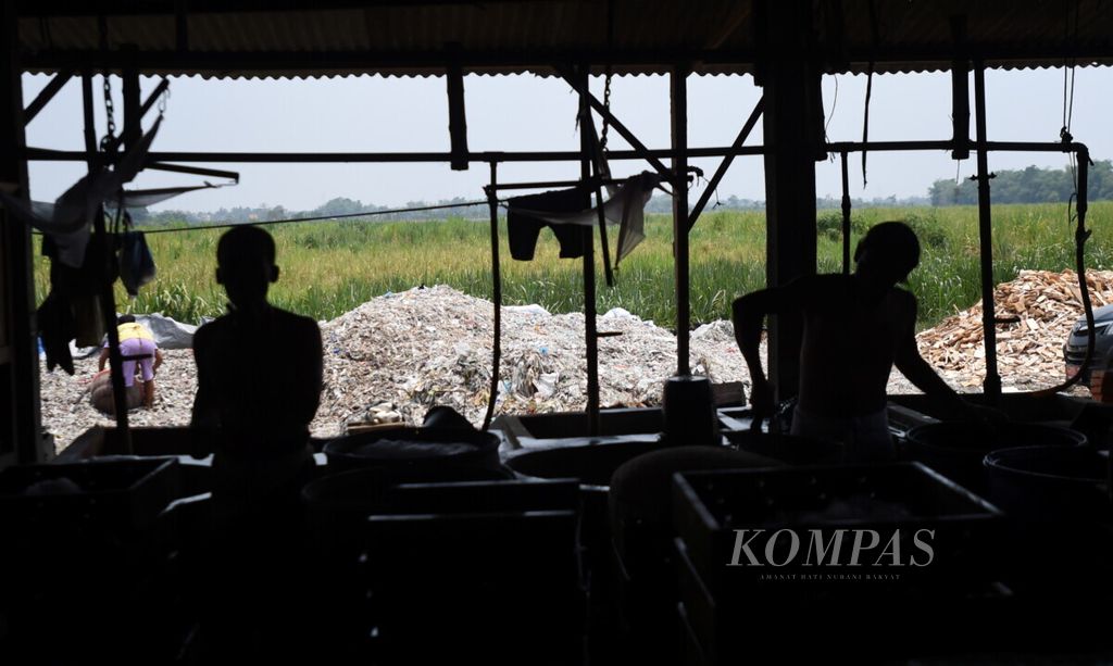 Siluet pekerja yang sedang mengolah kedelai di sentra pembuatan tahu dengan bahan bakar plastik impor di Desa Tropodo, Kecamatan Krian, Sidoarjo, Jawa Timur, Selasa (26/11/2019). 