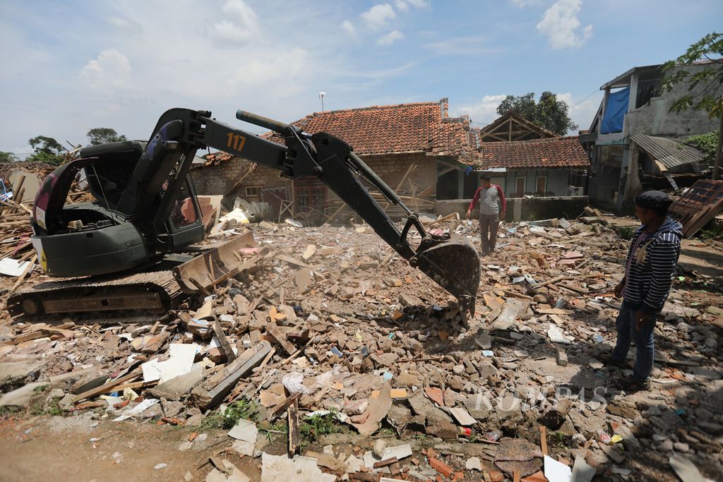 Petugas mengarahkan operator ekskavator saat membersihkan puing bangunan rumah warga di lokasi gempa di Kampung Cibulakan, Desa Cibulakan, Kecamatan Cugenang, Kabupaten Cianjur, Jawa Barat, Minggu (4/12/2022). 
