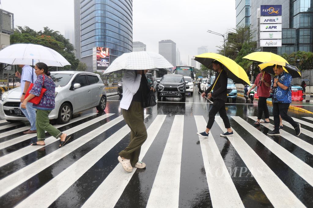 Pejalan kaki menggunakan payung saat menyeberang di Jalan Jenderal Sudirman, Jakarta, Jumat (19/1/2024) siang.