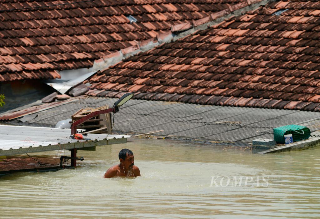 Warga berada di tengah banjir yang merendam rumah mereka hingga mencapai atap setelah jebolnya tanggul Sungai Wulan di Kecamatan Karanganyar, Kabupaten Demak, Jawa Tengah, Senin (12/2/2024). 