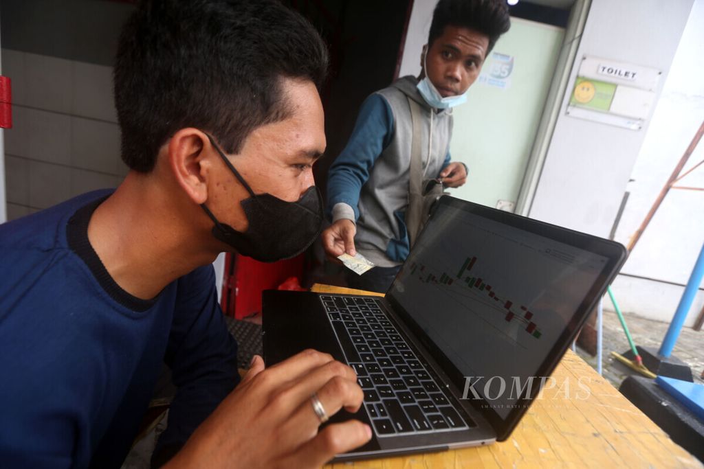 Surya memantau pergerakan harga saham miliknya dengan laptop yang terkoneksi dengan internet sembari bekerja sebagai penjaga toilet umum di kawasan Jakarta Barat, Rabu (3/2/2021). 