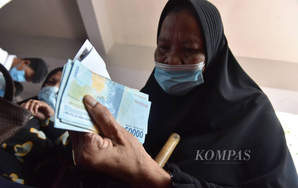 Warga memegang uang yang didapat saat penyaluran bantuan Program Keluarga Harapan, Bantuan Pangan Non Tunai, dan Bantuan Langsung Tunai minyak goreng di Kantor Kecamatan Rungkut, Kota Surabaya, Jawa Timur, Sabtu (16/4/2022). 