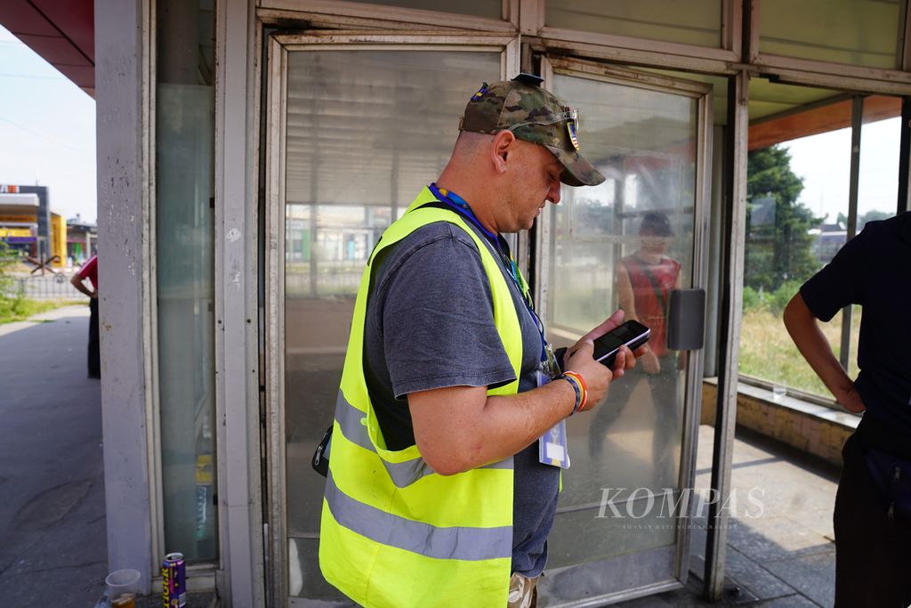 Jakub Jaworski (41), sukarelawan kemanusiaan asal Polandia, mengecek telepon selulernya di depan sebuah pintu menuju stasiun bawah tanah di Kharkiv, Ukraina, Kamis (7/7/2022). 