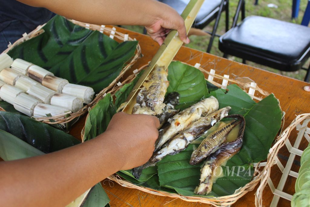 Ikan baung yang dicampur tempoyak dikeluarkan dari wadah bambu yang sebelumnya dibakar terlebih dahulu, pada Minggu (26/2023). Di sebelahnya terdapat nasi yang ditanak menggunakan daun lalu dibakar.