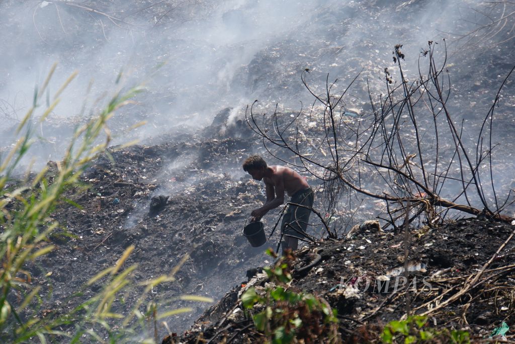 Warga membersihkan sampah di tengah kabut asap yang menyelimuti wilayah sekitar Tempat Pembuangan Akhir (TPA) Sumompo di daerah Tuminting, Manado, Sulawesi Utara, pada Rabu (4/10/2023).