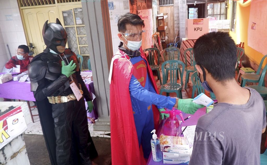 Anggota KPPS berkostum pahlawan super memeriksa suhu tubuh warga yang hendak memilih di TPS 15 Kelayan Timur, Kecamatan Banjarmasin Selatan, Kota Banjarmasin, Kalimantan Selatan, 9 Desember 2020. 