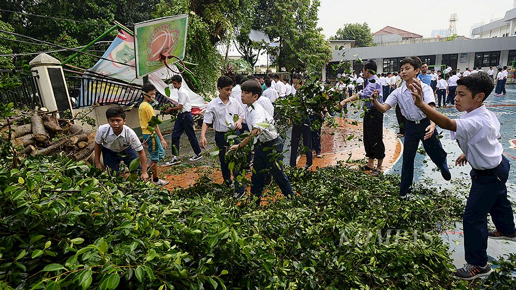 Siswa dan guru  bergotong royong menyingkirkan pohon yang tumbang di lapangan  SMP Muhammadiyah 8 Jakarta, Selasa (14/11). Hujan disertai angin kencang pada hari Senin (13/11)  membuat sejumlah pohon peneduh Jalan Bendi Besar, Jakarta Selatan, tumbang.