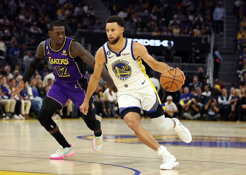 Pemain Golden State Warriors Stephen Curry mendribel bola melewati pemain LA Lakers Kendrick Nunn dalam pertandingan pembuka musim baru NBA antara LA Lakers dan Golden State Warriors di Chase Center, San Francisco, Rabu (19/10/2022) WIB. 