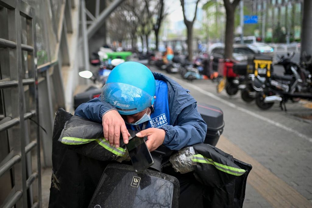 Seorang pekerja jasa pengantar tengah beristirahat di atas sepeda motor listrik miliknya di tepi jalan di Beijing. Foto diambil pada Sabtu (1/4/2023). 