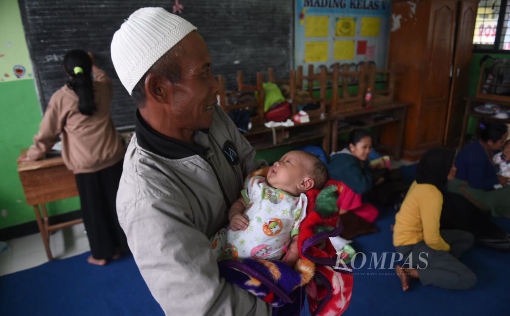 Dengan menggendong bayi, warga Dusun Umbulan mengungsi di SD Negeri Supiturang 4 pascaerupsi Gunung Semeru, Kecamatan Pronojiwo, Kabupaten Lumajang, Jawa Timur, Minggu (4/12/2022). 