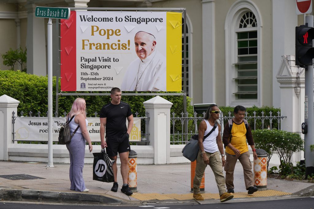 Orang-orang berjalan di depan poster bergambar Paus Fransiskus menjelang kunjungan Paus ke Singapura, Selasa (10/9/2024). Paus Fransiskus akan tiba di Singapura, Rabu (11/9/2024). 