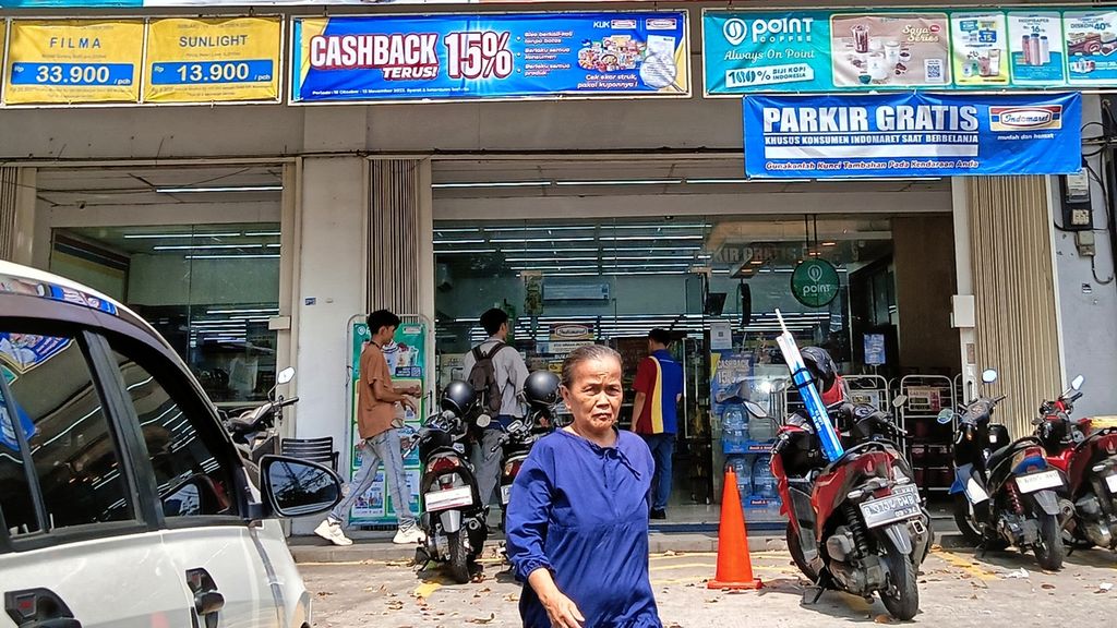 Seorang ibu baru saja keluar dari salah satu minimarket di Kebon Jeruk, Jakarta Barat, Senin (23/10/2023). Di minimarket itu tertulis parkir gratis.