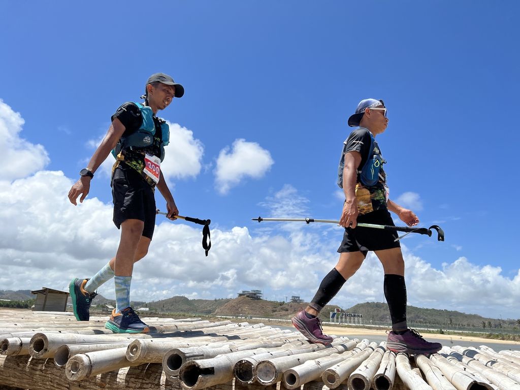 Dua peserta asal Padang, Sumatera Barat, melewati jembatan bambu di kawasan Pantai Seger saat mengikuti ajang Mandalika Ultra Trail 100 di Kawasan Ekonomi Khusus (KEK) Mandalika, Pujut, Lombok Tengah, Nusa Tenggara Barat, Sabtu (3/9/2022). Ajang yang pada 2022 memasuki tahun kedua penyelenggaraan ini bertujuan untuk mendukung pengembangan Mandalika sebagai kawasan <i>sport tourism</i>. Tidak hanya dari dalam negeri, peserta Mandalika 100 juga berasal dari luar negeri.