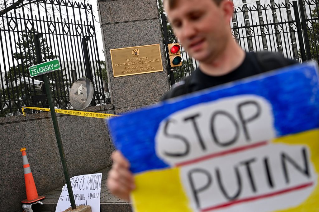  Seorang pengunjuk rasa memegang poster protes berbunyi "Stop Putin" di luar Kedutaan Besar Rusia, di depan tanda jalan tiruan yang menamai jalan tersebut dengan nama Presiden Ukraina Volodymyr Zelenskyy, di Washington, DC, Amerika Serikat, Senin (7/3/2022). 
