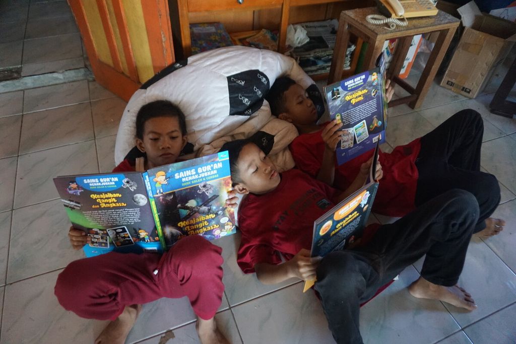 Arjun Dwi Antoro (8) dan teman-temannya rebahan membaca buku di kursi santai di Perpustakaan Bergerak Limbah Pustaka di Desa Muntang, Kecamatan Kemangkon, Kabupaten Purbalingga, Jawa Tengah, Minggu (30/4/2023).