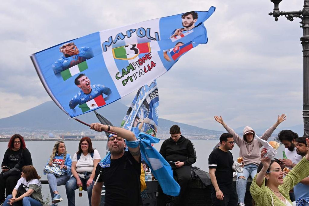 Para pendukung Napoli bersiap untuk berpesta di tepi pantai dengan latar belakang Gunung Vesuvius saat berlangsungnya laga Liga Italia antara Napoli dan Salernitana di Stadion Diego Maradona, Napoli, Minggu (30/4/2023). 