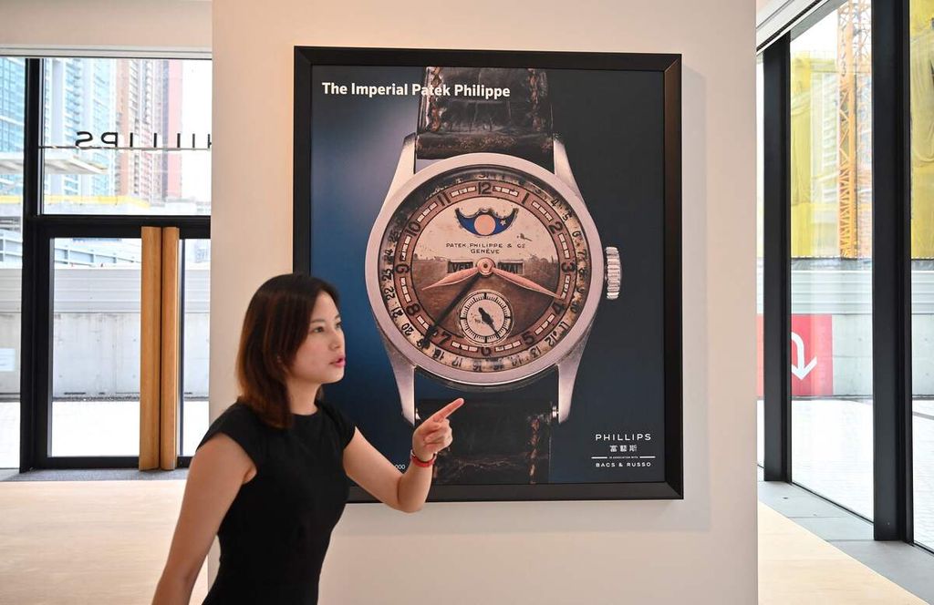 Seorang perempuan berdiri di depan poster bergambar jam tangan Patek Philippe Ref 96 Quantieme Lune, yang pernah dimiliki kaisar terakhir China dari Dinasti Qing, Aisin-Gioro Puyi, di rumah bursa Phillips, Hong Kong, Selasa (23/5/2023).  
