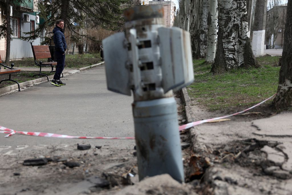 Seorang pria berjalan melewati bagian ekor roket 300 mm yang tidak meledak  yang diluncurkan dari peluncur roket ganda BM-30 Smerch yang tertanam di tanah setelah penembakan di Lysychansk, wilayah Lugansk, Ukraina (11/4/2022).