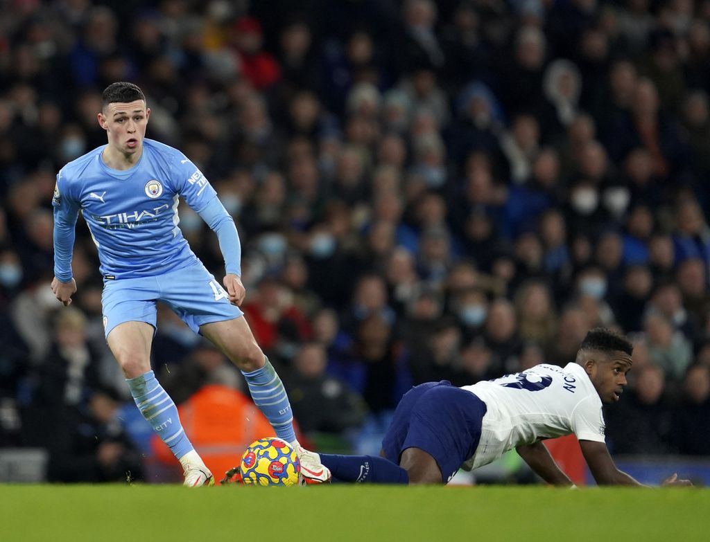 Pemain Manchester City, Phil Foden (kiri), menggiring bola melewati pemain Tottenham Hotspur, Ryan Sessegnon, dalam pertandingan Liga Inggris di Stadion Etihad, Manchester, Minggu (20/2/2022) dini hari WIB.