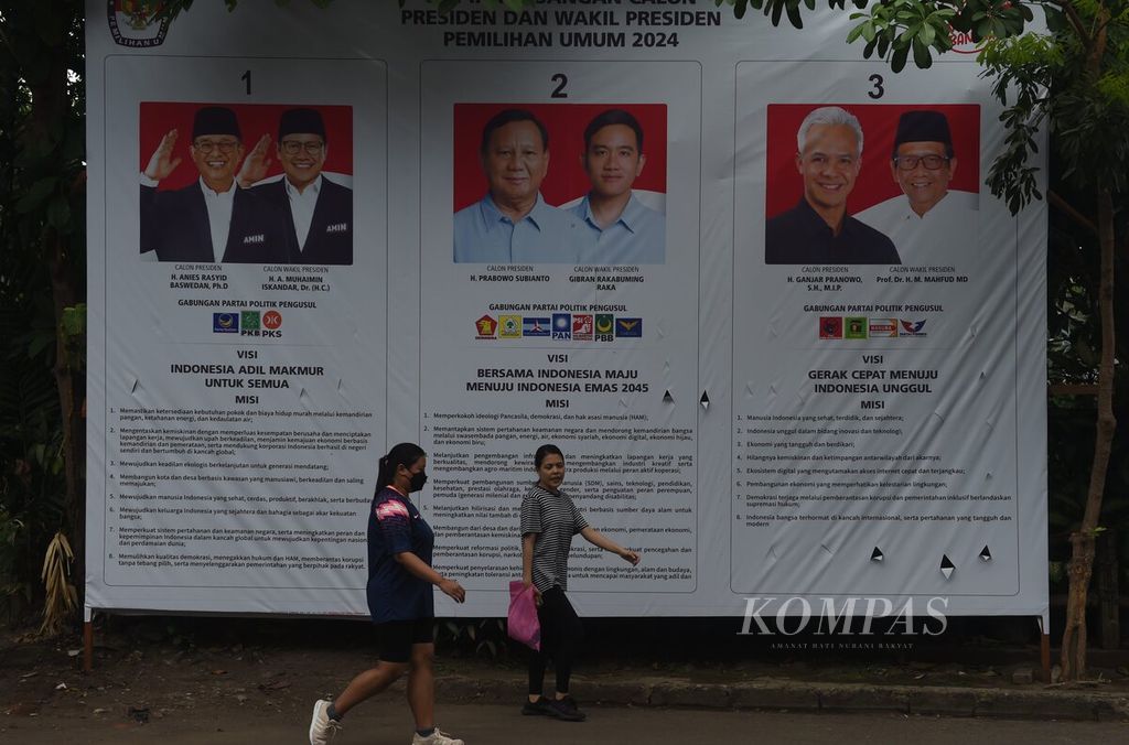 Warga melewati baliho resmi KPU yang memuat visi-misi pasangan calon presiden dan calon wakil presiden dalam Pemilihan Umum 2024 di Jalan Kayoon, Surabaya, Jawa Timur, Minggu (17/12/2023).  