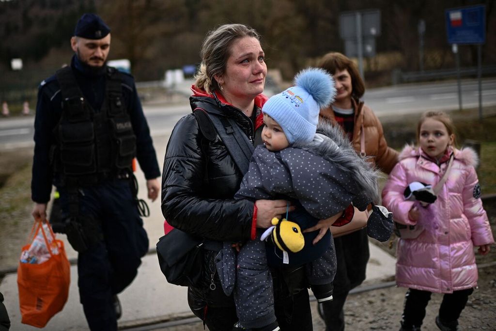 Seorang perempuan pengungsi Ukraina menggendong bayinya, dikawal seorang polisi penjaga perbatasan Polandia (kiri), menyeberangi perbatasan dari Ukraina menuju Polandia di pintu perbatasan Kroscienko, Kamis (7/4/2022).
