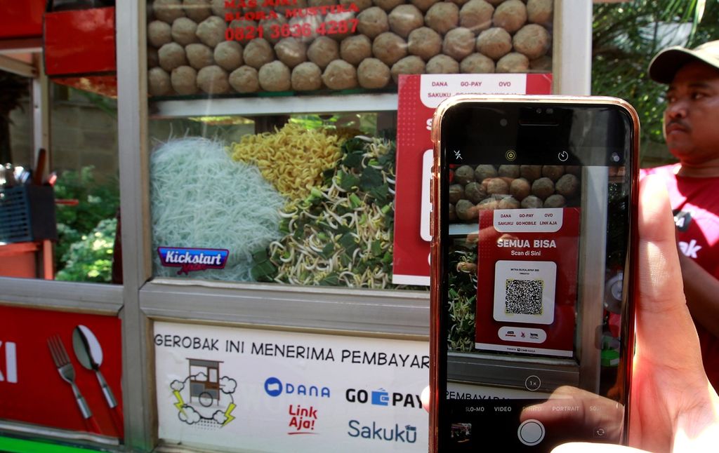 Maman (40), pedagang bakso di daerah Kemang Raya, Jakarta, Rabu (21/8/2019), menerima pembayaran melalui Quick Response Code Indonesian Standard (QRIS) dari para pembelinya. QRIS dapat diakses menggunakan uang elektronik berbasis server, seperti DANA, LinkAja, Gopay, dan OVO.
